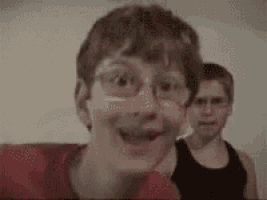 a woman wearing glasses is making a funny face in front of a man wearing a black tank top .