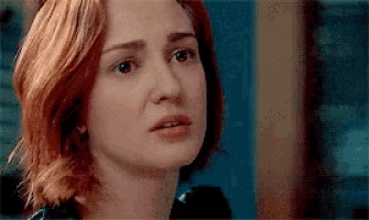 a woman with red hair is looking at the camera with a serious look on her face .