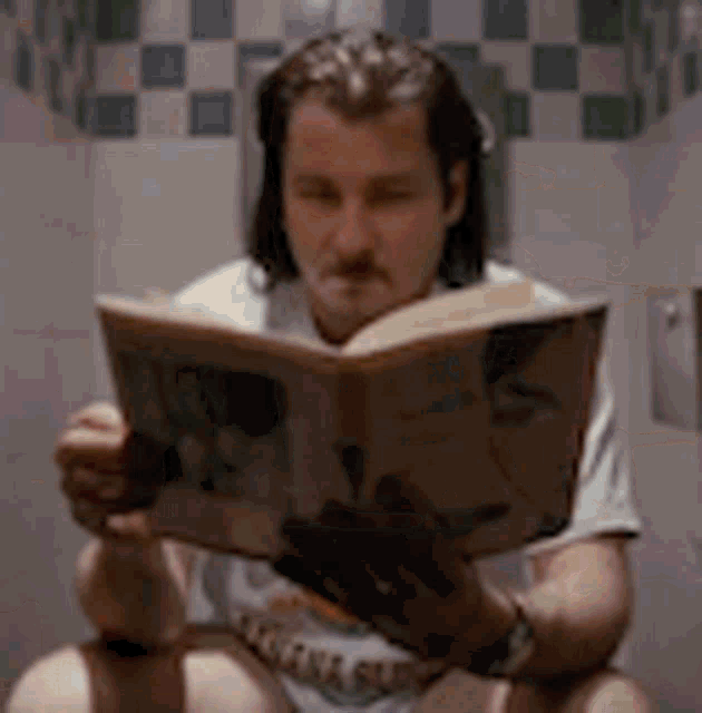 a man is sitting on a toilet while reading a book .