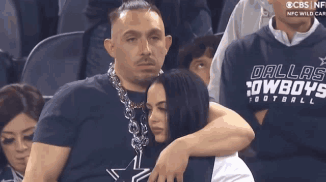a man wearing a dallas cowboys football shirt is hugging a woman