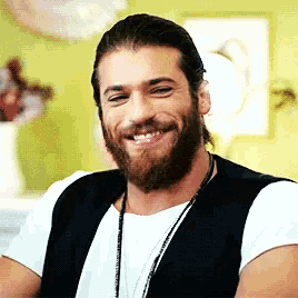 a man with a beard is smiling and wearing a white shirt and a black vest