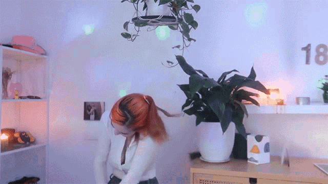 a woman with red hair is dancing in front of a plant and a sign that says 18