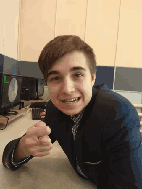 a young man sitting at a desk with a computer monitor in the background