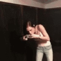 a woman in a bra and jeans is standing in a dark room drinking from a cup .