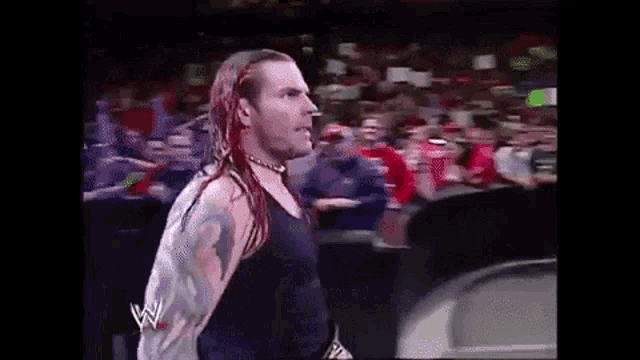 a wrestler with red hair and dreadlocks is standing in front of a crowd .