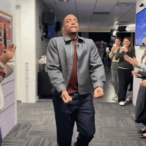 a man in a grey jacket is dancing in a hallway with people clapping