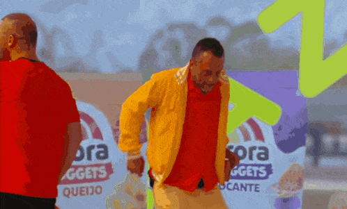a man in a yellow jacket is dancing in front of a sign that says ora nuggets queijo