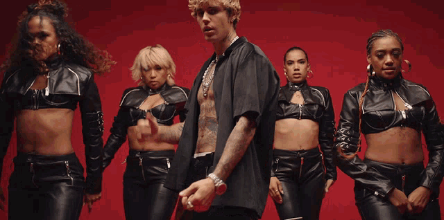 a man in a black shirt stands in front of a group of women in black leather outfits