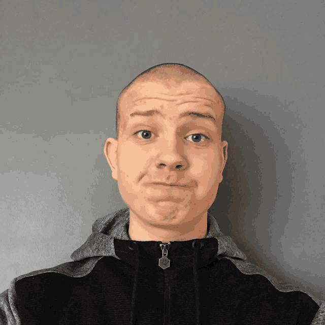 a man with a shaved head is wearing a grey and black jacket