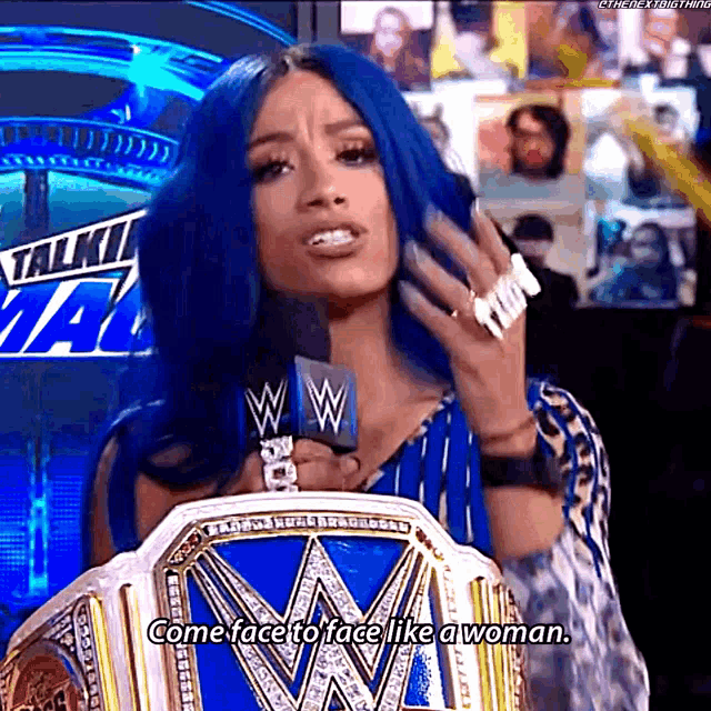 a woman with blue hair is holding a wrestling championship belt while talking into a microphone .