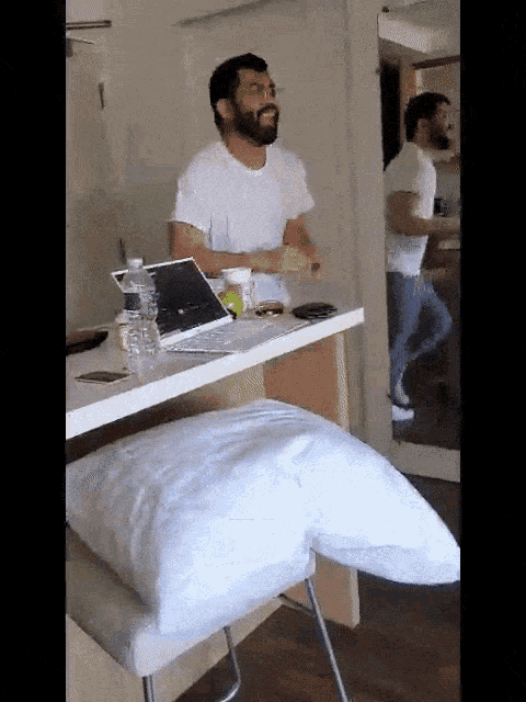 a man sitting at a table with a laptop and a pillow