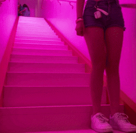 a woman is standing on a set of stairs with a pink light behind her