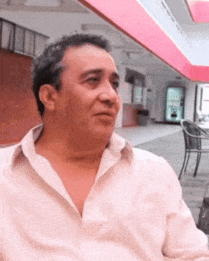 a man wearing a white shirt is sitting in front of a pink building
