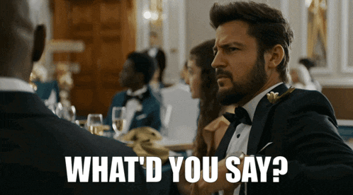 a man in a tuxedo is sitting at a table and says what 'd you say