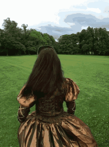 a woman in a brown and gold dress is running in a field