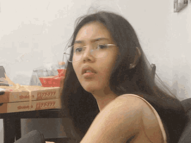 a woman wearing glasses sits in front of a stack of pizza boxes that say shakey 's on them