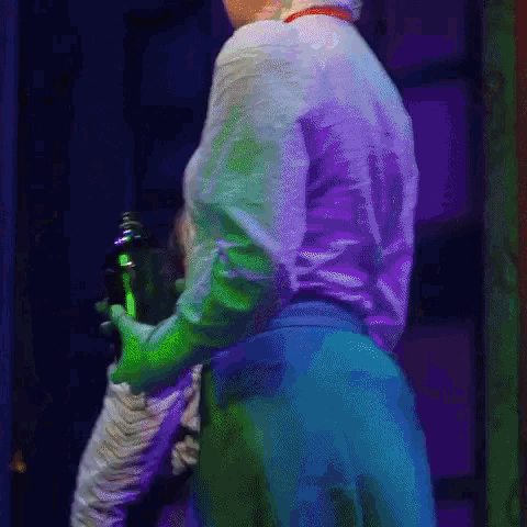 a woman in a white shirt and blue pants is standing on a stage in a dark room holding a green object .