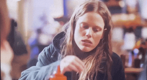 a woman in a blue hoodie is pouring ketchup into her mouth