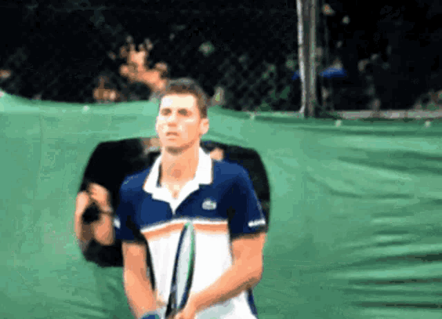 a man in a lacoste shirt is holding a tennis racquet on a tennis court