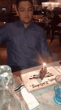 a man in a blue shirt is sitting at a table with a birthday cake