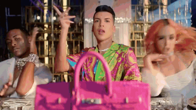 a man in a colorful shirt is holding a pink purse while dancing with two other people .
