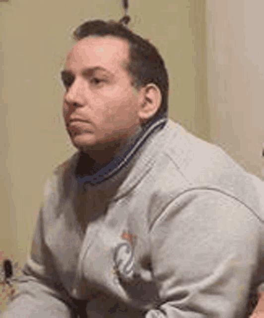 a man in a gray sweatshirt is sitting in a room .