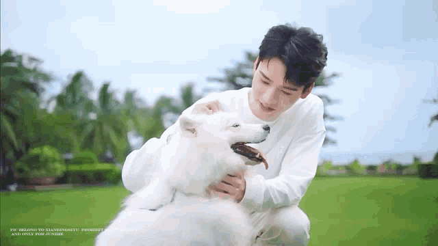 a man in a white sweater is petting a white dog in a field .