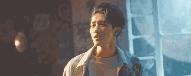 a young man is standing in front of a window in a dark room and looking out the window .