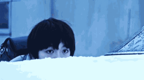 a young boy is peeking out from behind a car windshield in the snow .