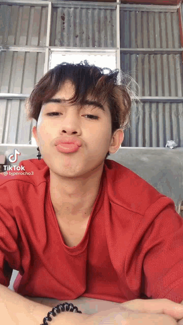 a young man wearing a red shirt is making a funny face with his tongue out