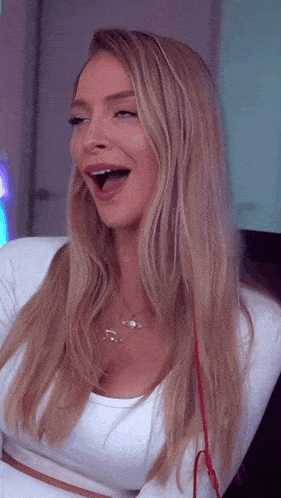 a blonde woman wearing a white top and a necklace with music notes