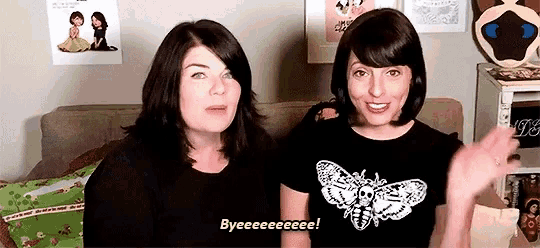 two women are sitting next to each other on a couch and one of them is wearing a shirt that says bye .