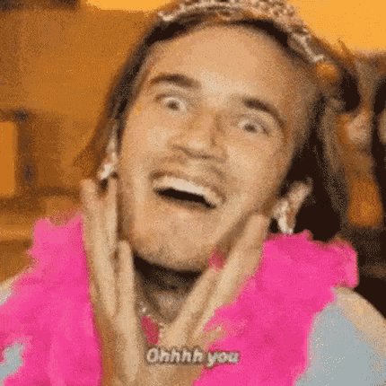 a man wearing a pink boa and a tiara is smiling and making a funny face .