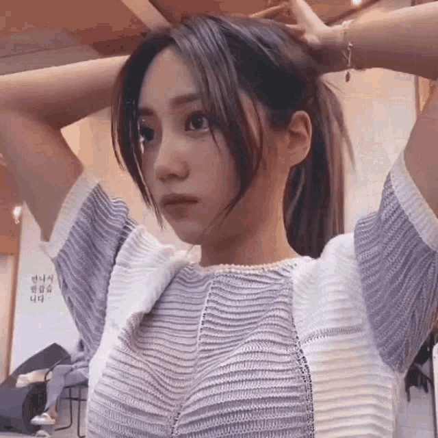 a woman is holding her hair in a ponytail while wearing a sweater and a pearl necklace .