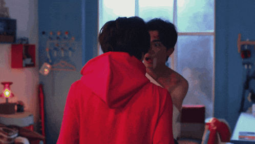 a man in a red hoodie is standing next to a shirtless man