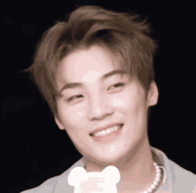 a young man wearing a pearl necklace is smiling and looking at the camera .