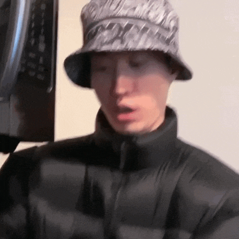 a man wearing a bucket hat and a black jacket is standing in front of a tv .
