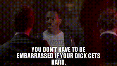 a man in a suit is talking to another man in a dark room while another man watches .