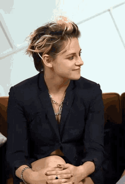 a woman in a black suit sits on a couch with her legs crossed