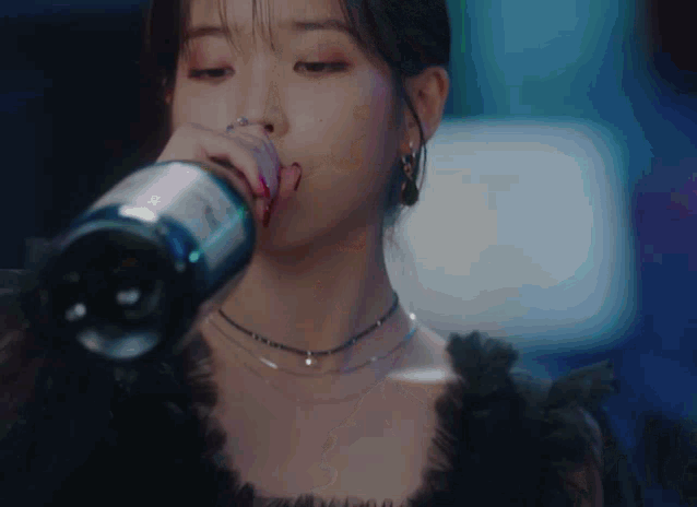 a woman in a black dress is drinking from a bottle that says ' a ' on it