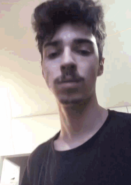a young man with a beard is wearing a black shirt and looking at the camera .