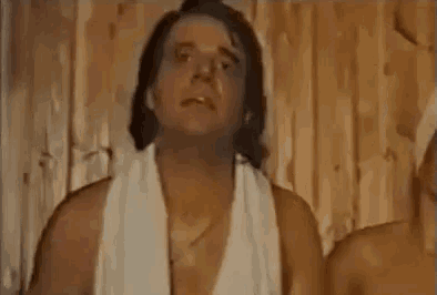 a man with a towel around his neck is standing in front of a wooden wall and says che ansia tremenda .