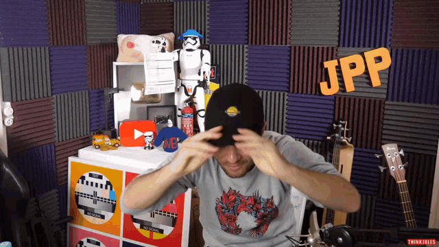 a man adjusts his hat in front of a wall that says jpp