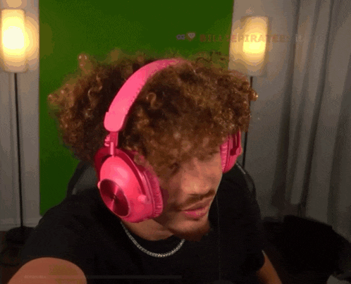 a man with curly hair wearing pink headphones with a green screen in the background