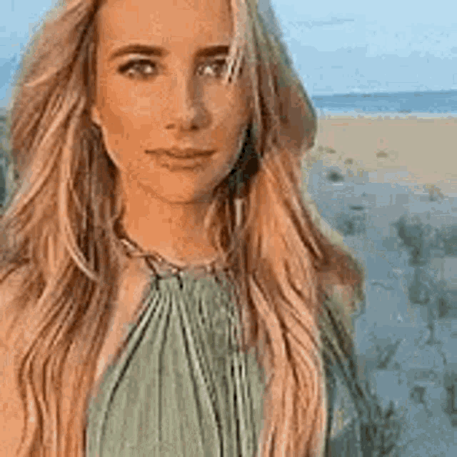 a woman in a green dress is standing on a beach looking at the camera .
