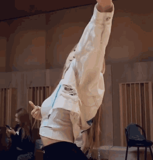 a woman in a white jacket is dancing in a room with her arms outstretched .