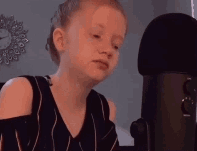 a young girl is sitting in front of a microphone making a funny face .