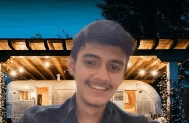 a young man with a mustache is smiling in front of a house .
