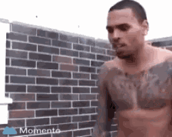 a man without a shirt is standing in front of a brick wall .