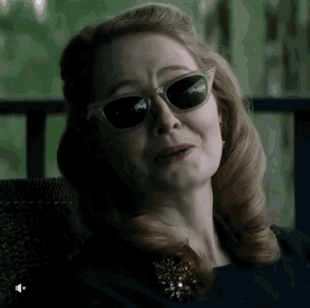 a woman wearing sunglasses is sitting in a chair and making a funny face